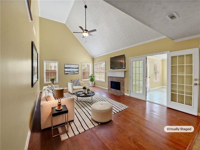 living area featuring high vaulted ceiling, a tile fireplace, wood finished floors, visible vents, and a ceiling fan