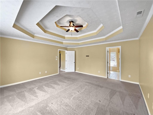 empty room featuring carpet floors, visible vents, a tray ceiling, and a ceiling fan
