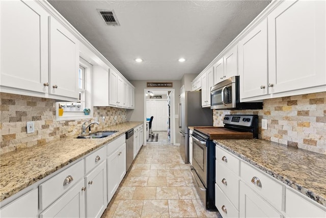 kitchen with visible vents, a sink, appliances with stainless steel finishes, white cabinetry, and tasteful backsplash