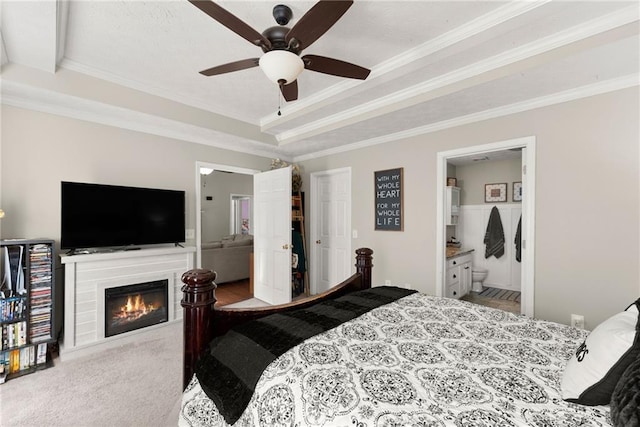 bedroom featuring a glass covered fireplace, a raised ceiling, crown molding, and carpet floors