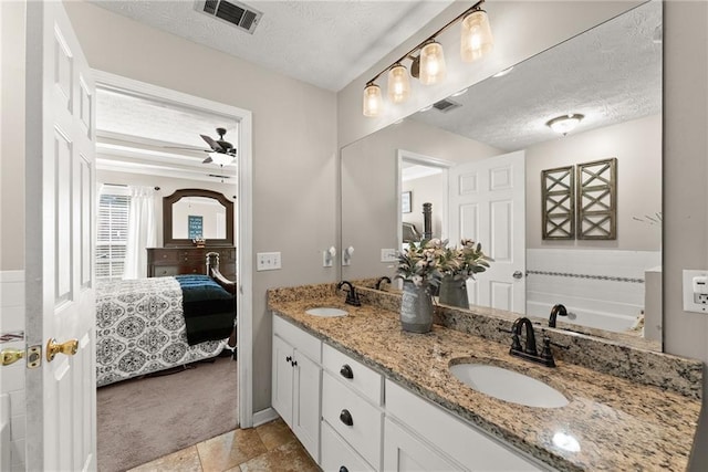 ensuite bathroom with a textured ceiling, connected bathroom, visible vents, and a sink