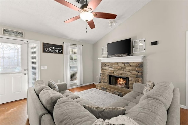 living area featuring wood finished floors, baseboards, lofted ceiling, ceiling fan, and a stone fireplace