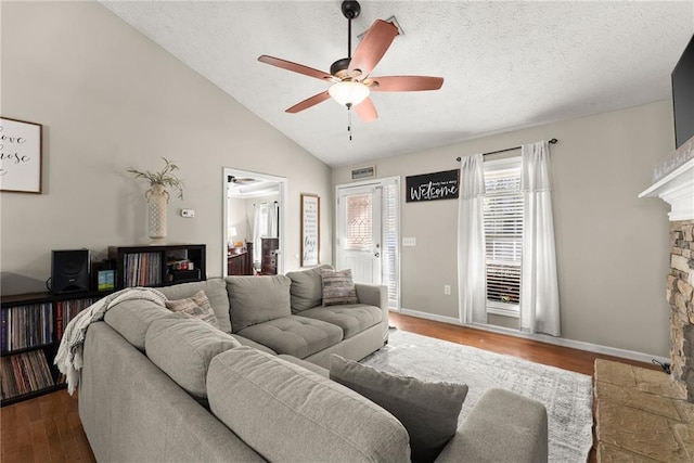 living room featuring a ceiling fan, a textured ceiling, wood finished floors, a fireplace, and lofted ceiling