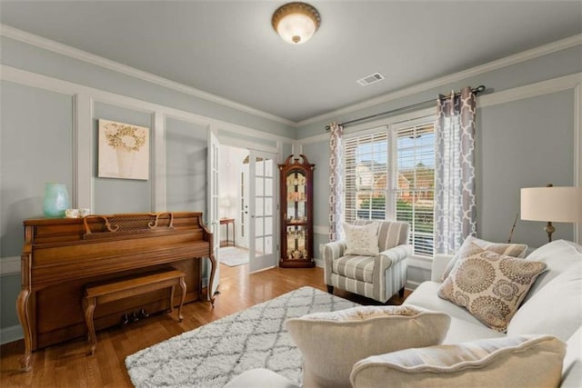 living area with french doors, visible vents, crown molding, and wood finished floors