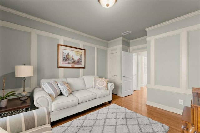 living area with visible vents, crown molding, baseboards, and wood finished floors