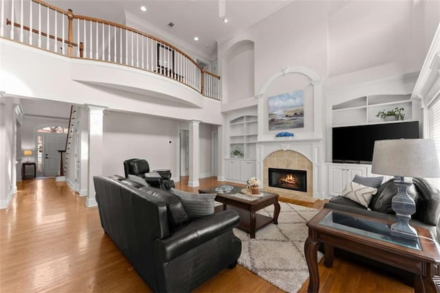 living room featuring built in features, baseboards, a tiled fireplace, light wood-style flooring, and ornate columns