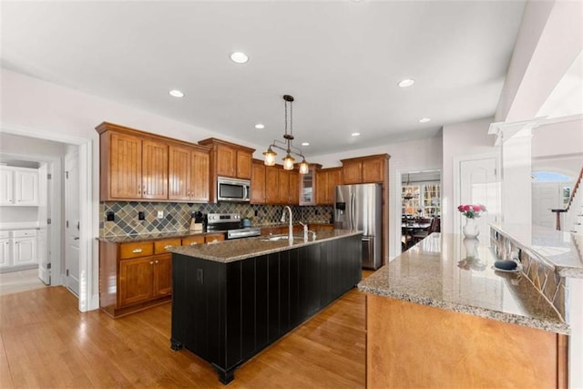 kitchen with hanging light fixtures, brown cabinetry, a kitchen island with sink, and stainless steel appliances