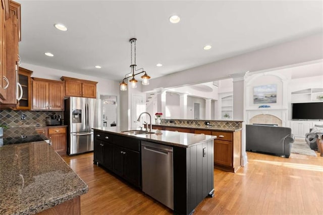 kitchen featuring a sink, appliances with stainless steel finishes, brown cabinets, a center island with sink, and pendant lighting