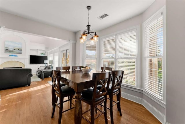 dining space featuring baseboards, wood finished floors, visible vents, and an inviting chandelier