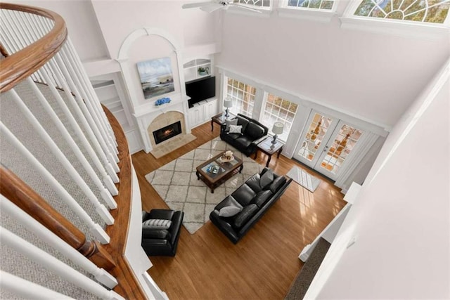 living area with built in features, a towering ceiling, ceiling fan, wood finished floors, and a lit fireplace