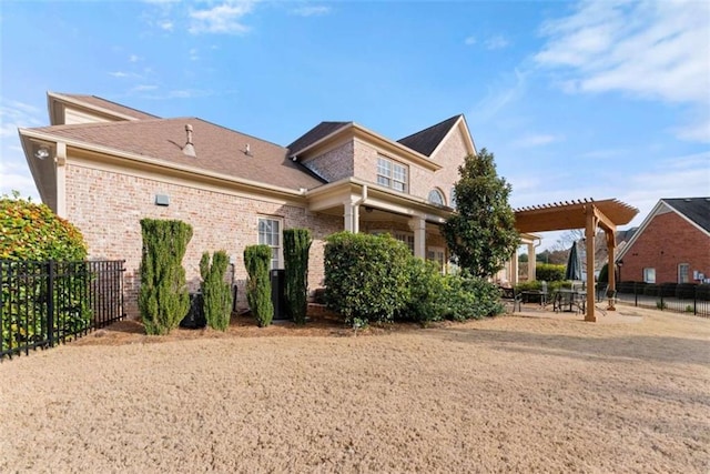 view of front of property featuring brick siding, a patio area, fence, and a pergola