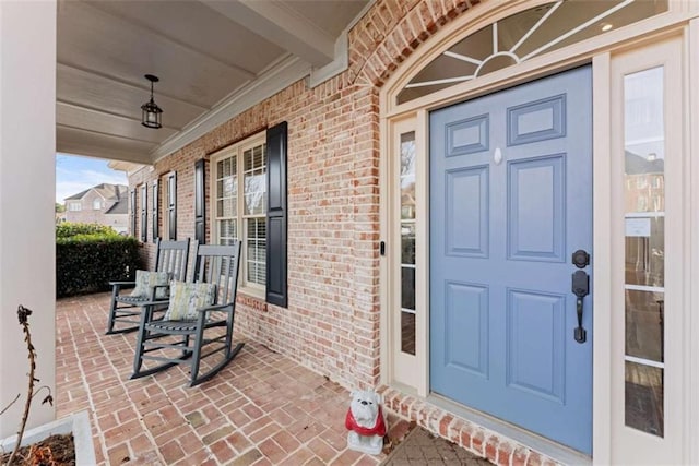 entrance to property with a porch and brick siding