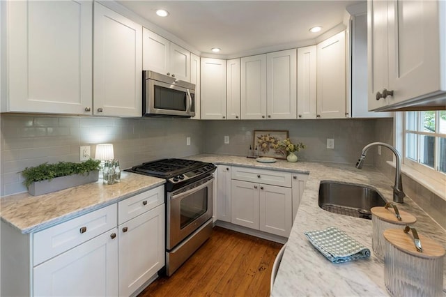 kitchen with appliances with stainless steel finishes, a sink, dark wood-type flooring, white cabinets, and recessed lighting