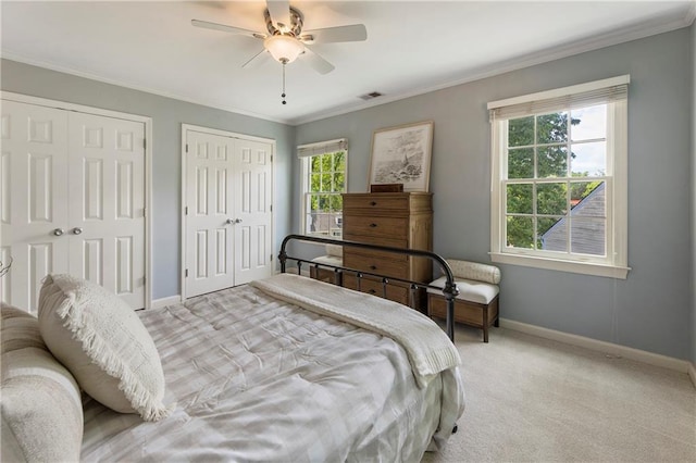 carpeted bedroom featuring multiple closets, baseboards, ornamental molding, and ceiling fan