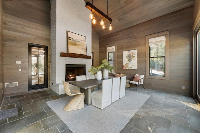 unfurnished dining area with wood walls, wooden ceiling, high vaulted ceiling, and a large fireplace