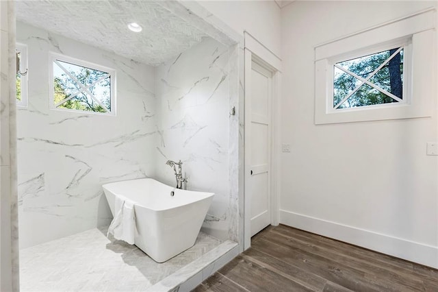 bathroom featuring a wealth of natural light, a textured ceiling, wood-type flooring, and a bathing tub