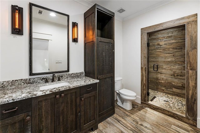 bathroom featuring a shower with door, hardwood / wood-style floors, toilet, vanity, and crown molding