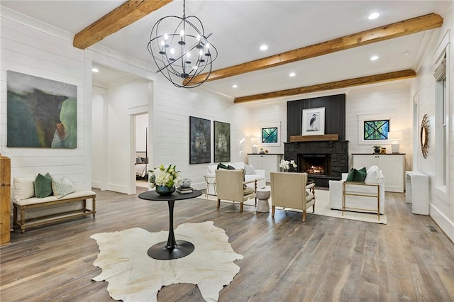 living room featuring a stone fireplace, a notable chandelier, hardwood / wood-style floors, and beam ceiling