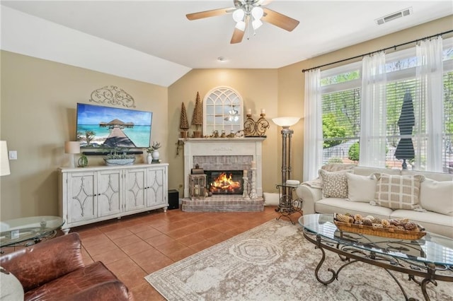 tiled living room featuring a brick fireplace, ceiling fan, visible vents, and lofted ceiling