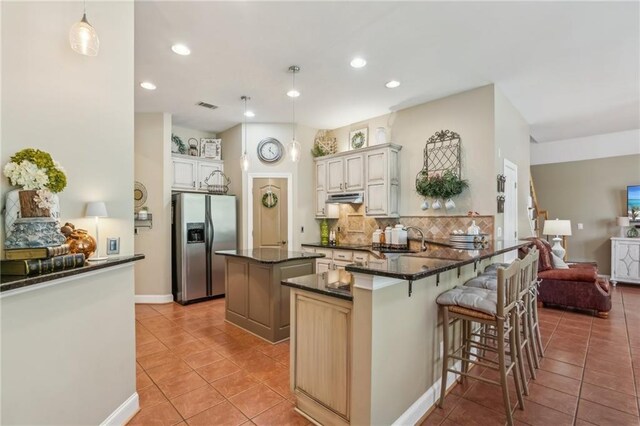 kitchen featuring visible vents, a kitchen island, stainless steel refrigerator with ice dispenser, under cabinet range hood, and light tile patterned floors