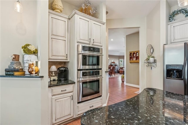 kitchen featuring backsplash, appliances with stainless steel finishes, light tile patterned floors, and dark stone countertops