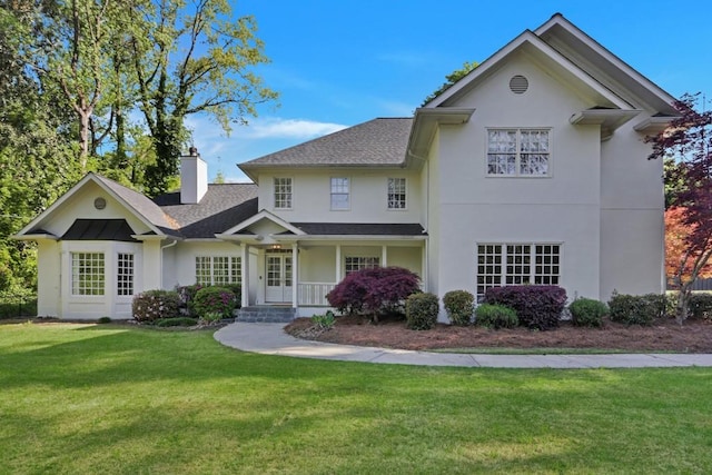 view of front of property with a front lawn, stucco siding, roof with shingles, and a chimney