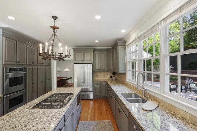 kitchen featuring gray cabinets, a sink, backsplash, wood finished floors, and appliances with stainless steel finishes