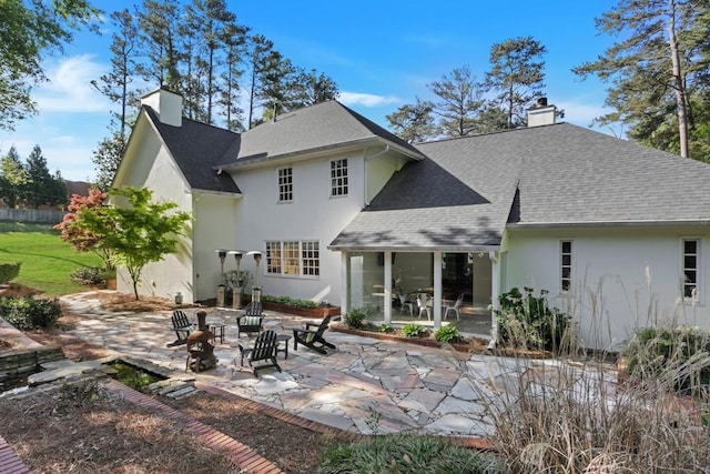 back of property featuring a patio area, stucco siding, a chimney, and roof with shingles