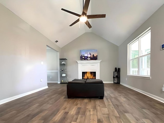 living area with baseboards, dark wood-type flooring, a lit fireplace, and vaulted ceiling