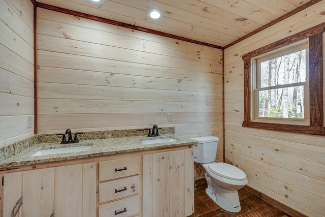 bathroom featuring toilet, double vanity, wooden walls, and a sink