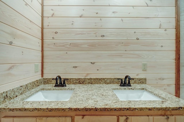 bathroom with a sink, wood walls, and double vanity