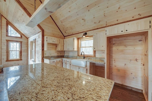 kitchen featuring wooden ceiling, vaulted ceiling, wood walls, light stone countertops, and a sink
