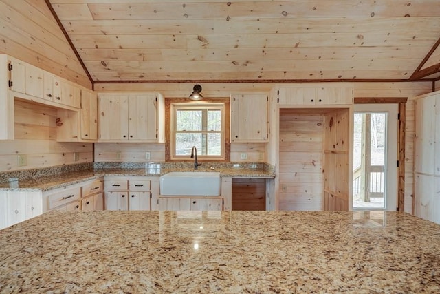 kitchen with a sink, light stone counters, wood walls, lofted ceiling, and wooden ceiling