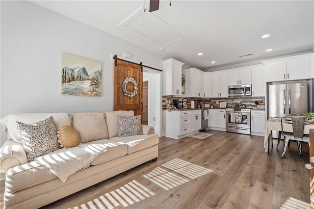 living room featuring ceiling fan, a barn door, sink, and hardwood / wood-style floors