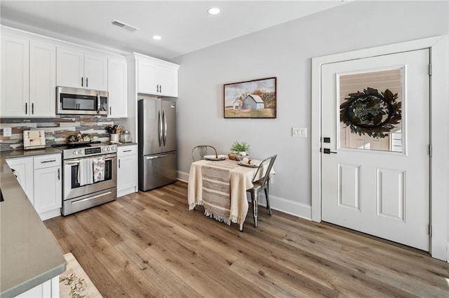 kitchen with decorative backsplash, appliances with stainless steel finishes, white cabinetry, and light hardwood / wood-style flooring