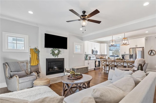 living room featuring ceiling fan with notable chandelier, a large fireplace, dark hardwood / wood-style floors, and crown molding