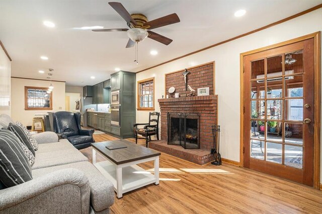 living room featuring ceiling fan, light hardwood / wood-style flooring, crown molding, and a brick fireplace