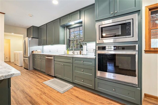 kitchen featuring appliances with stainless steel finishes, backsplash, sink, green cabinetry, and light hardwood / wood-style floors