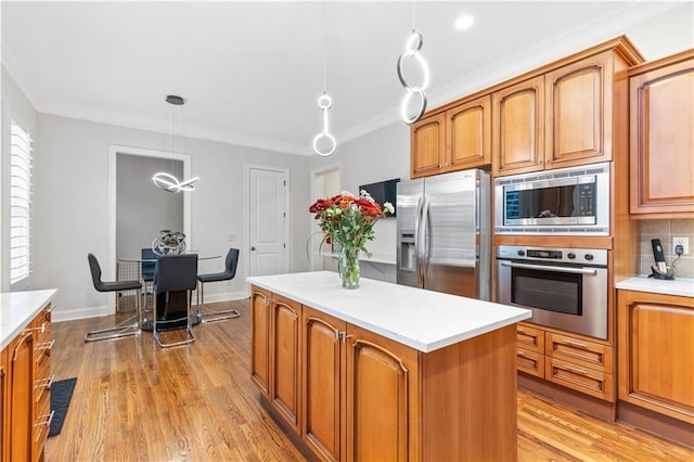 kitchen featuring stainless steel appliances, crown molding, hanging light fixtures, and light wood-type flooring