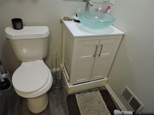 half bathroom featuring toilet, wood finished floors, vanity, and visible vents