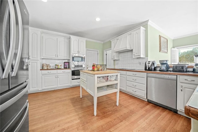 kitchen with white cabinetry, wood counters, tasteful backsplash, premium range hood, and appliances with stainless steel finishes