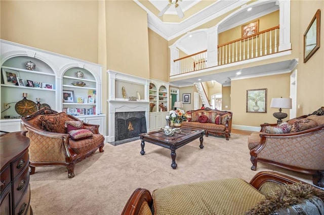 carpeted living room featuring ceiling fan, a high ceiling, built in features, a high end fireplace, and ornamental molding