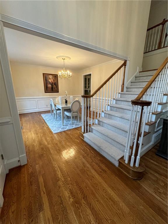 stairs featuring hardwood / wood-style floors, ornamental molding, and a notable chandelier