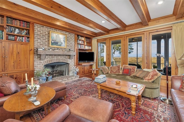 living room featuring built in shelves, crown molding, wood-type flooring, beamed ceiling, and a fireplace