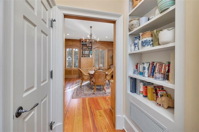 hall with built in features, a notable chandelier, and light hardwood / wood-style floors