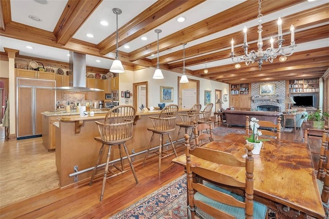 dining area with crown molding, beamed ceiling, light hardwood / wood-style floors, a brick fireplace, and a chandelier