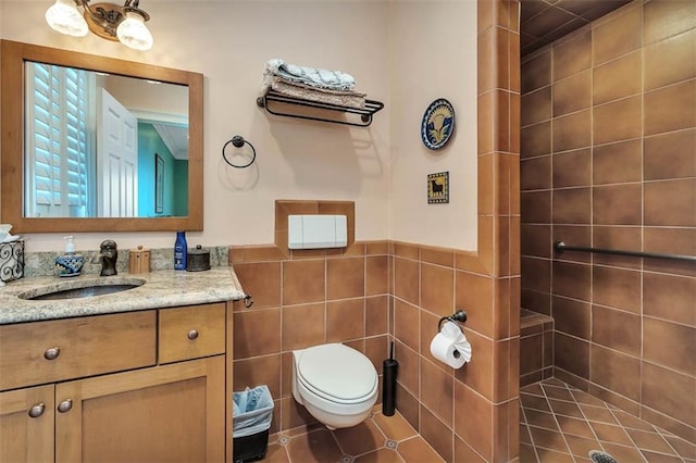 bathroom with tile walls, vanity, toilet, and a tile shower