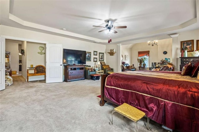 carpeted bedroom with a tray ceiling and ceiling fan with notable chandelier