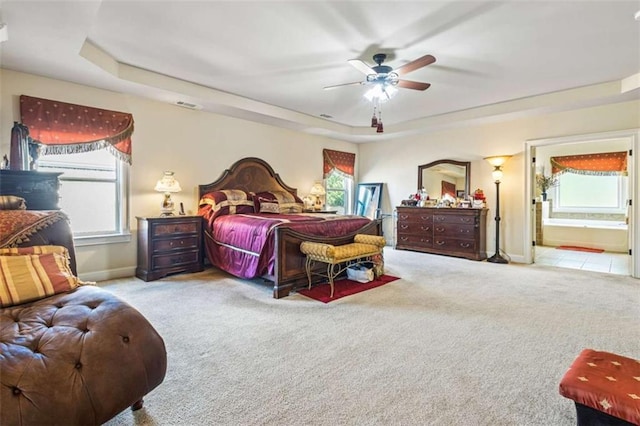 bedroom featuring a raised ceiling, ceiling fan, light colored carpet, and ensuite bath