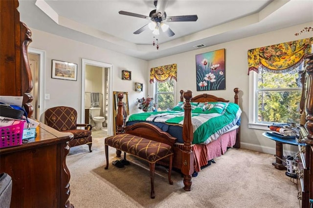 carpeted bedroom with a raised ceiling, ceiling fan, and ensuite bathroom